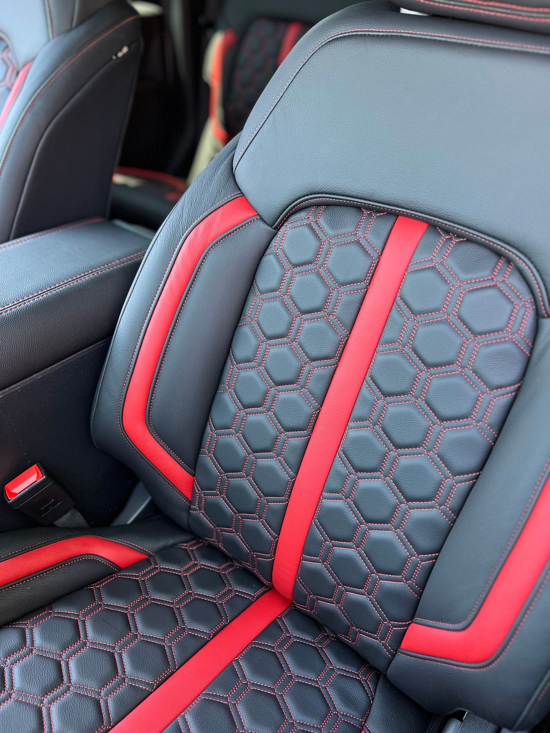Black car seat with red accents and hex-patterned center upholstery