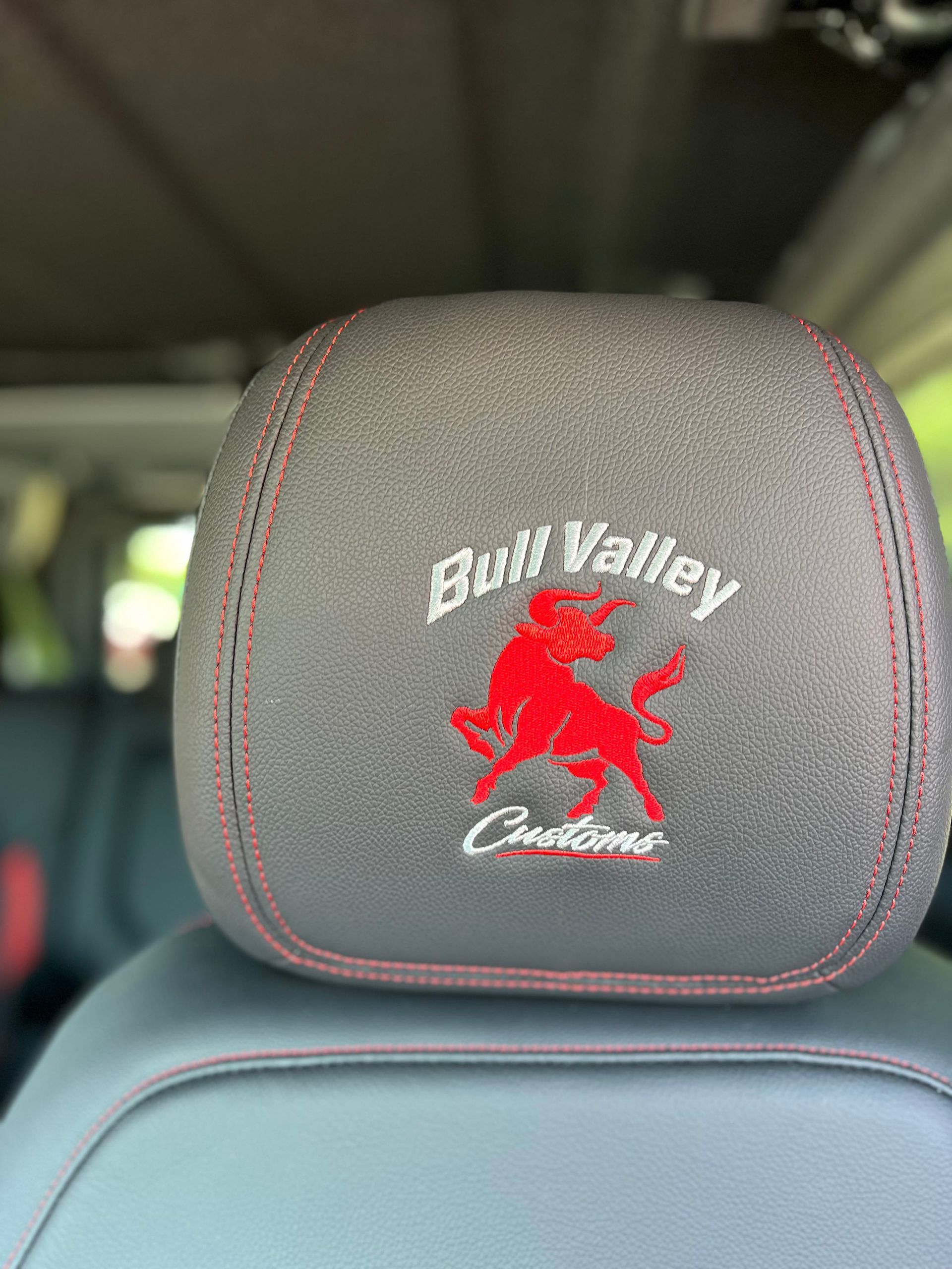 Gray embroidered car headrest with red buffalo and Bull Valley logo on black leather seat
