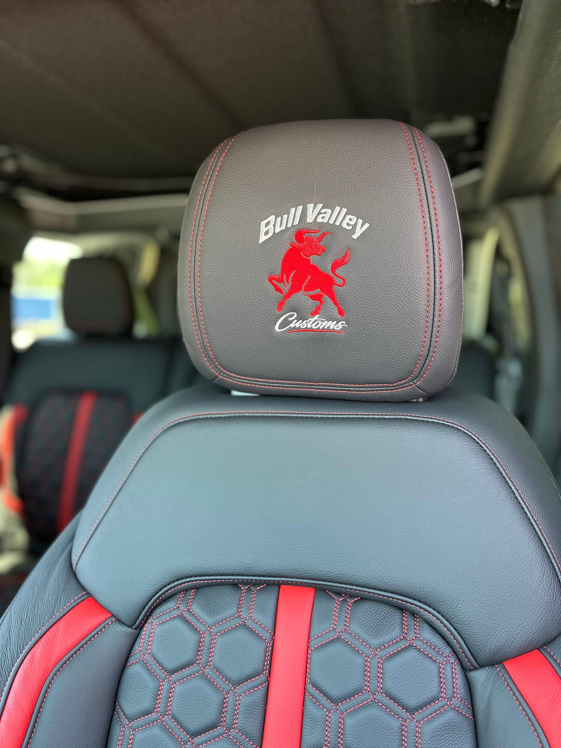 Car seat headrest with red-and-gray hex pattern and red logo embroidery, inside a vehicle