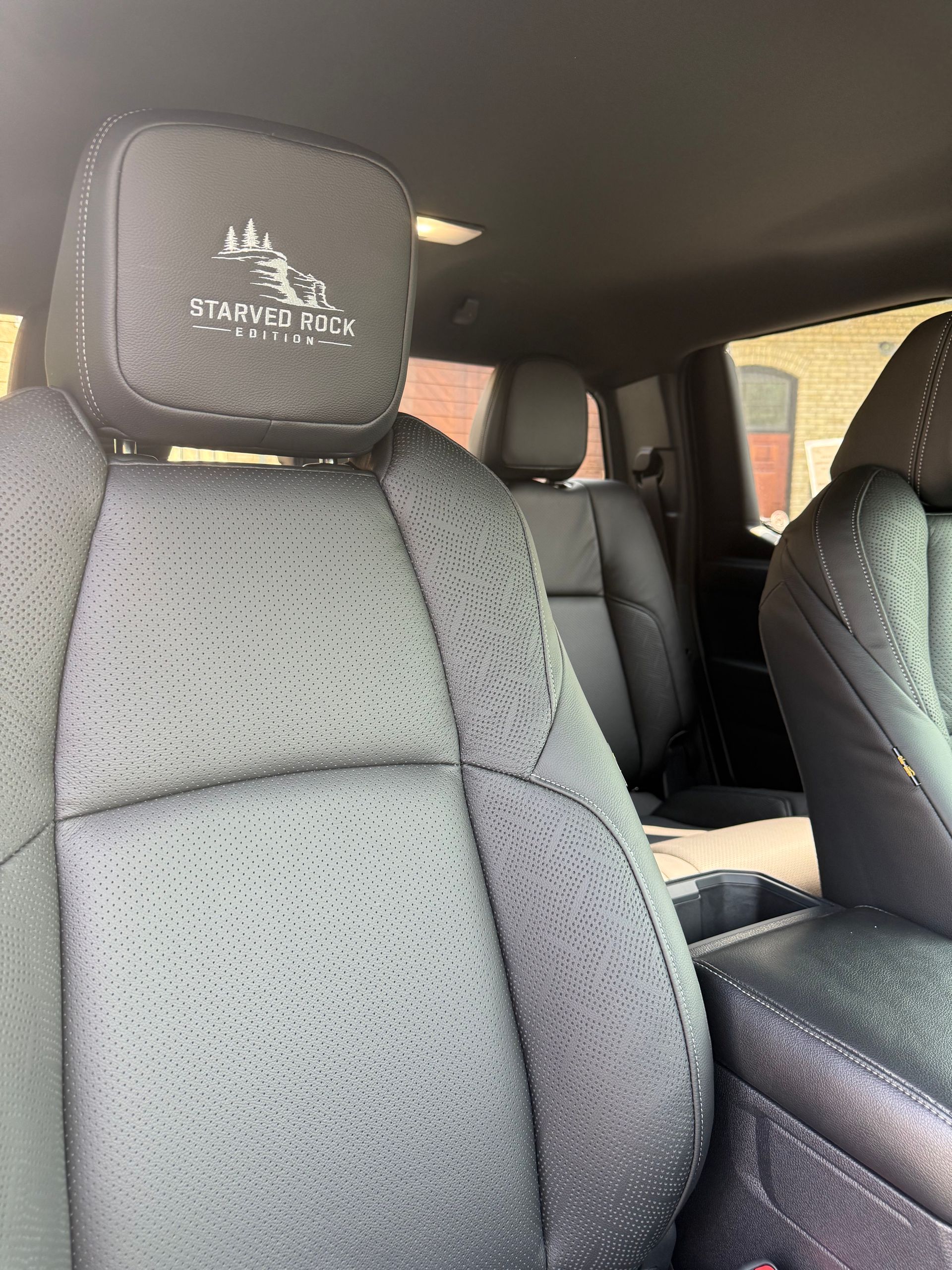 Car interior with black perforated seats and a front headrest embroidered with a tree logo.