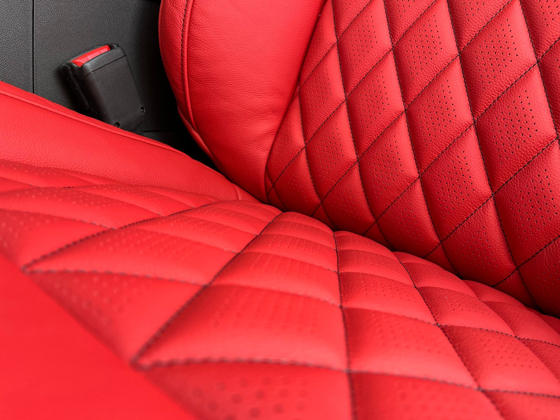 Red quilted car seats with black seatbelt buckle visible close up