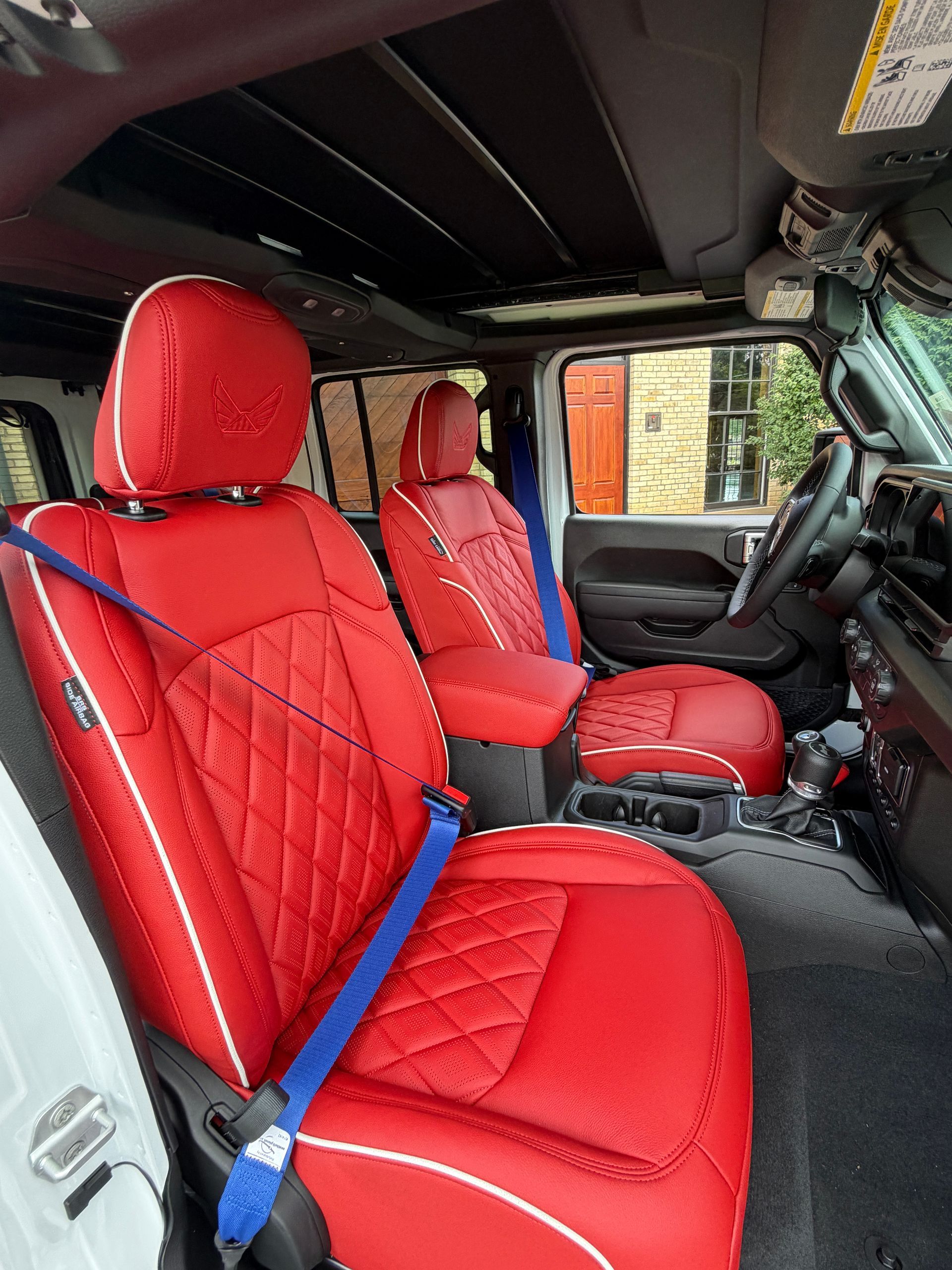 Red quilted car seats with blue seat belts inside a vehicle, viewed from the open door