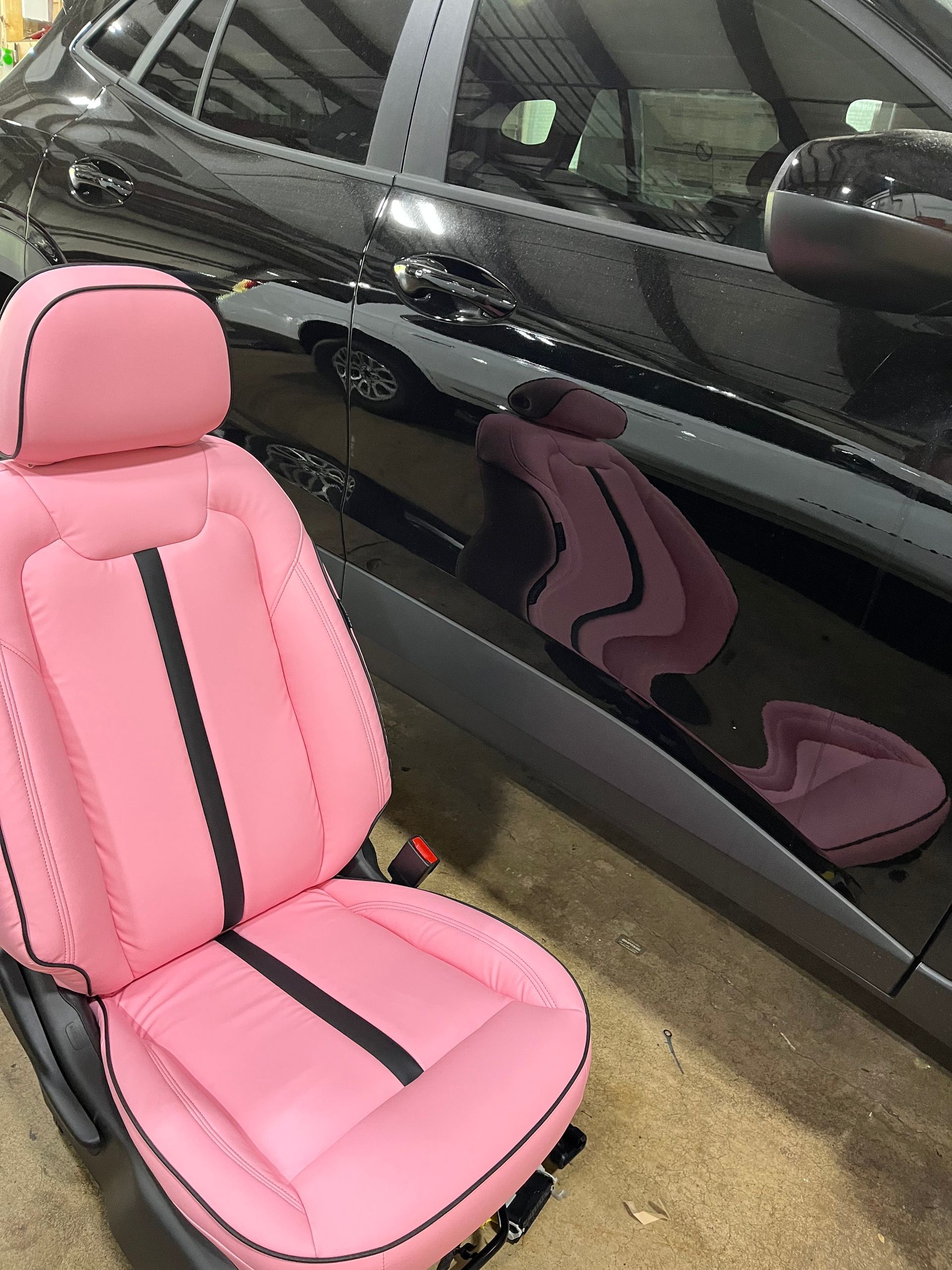 Pink car seat beside a black car, showing upholstery color contrast indoors.