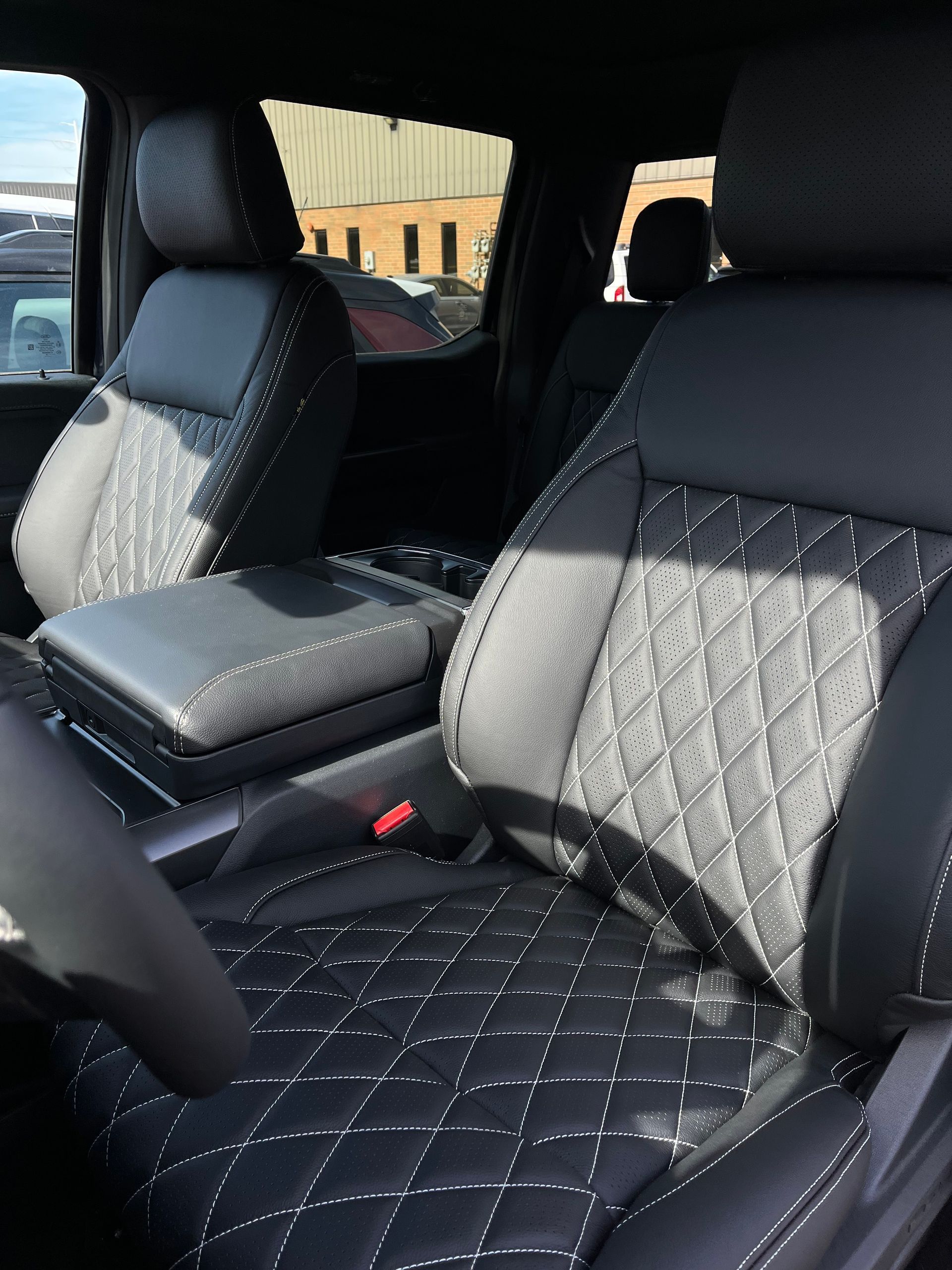 Quilted car seats and center console inside a vehicle, seen from the front passenger side.