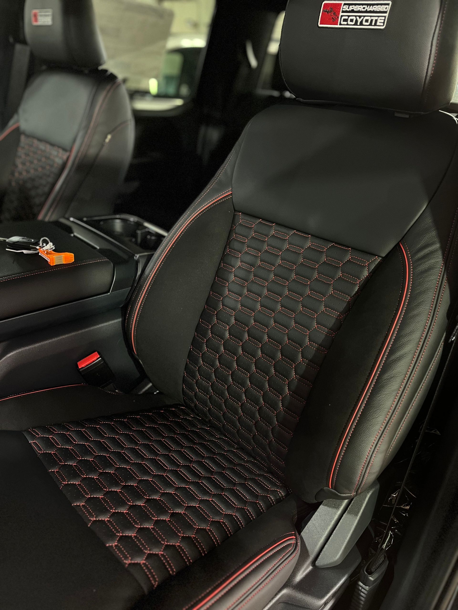Black car seat with red stitching and patterned center panel inside a vehicle interior