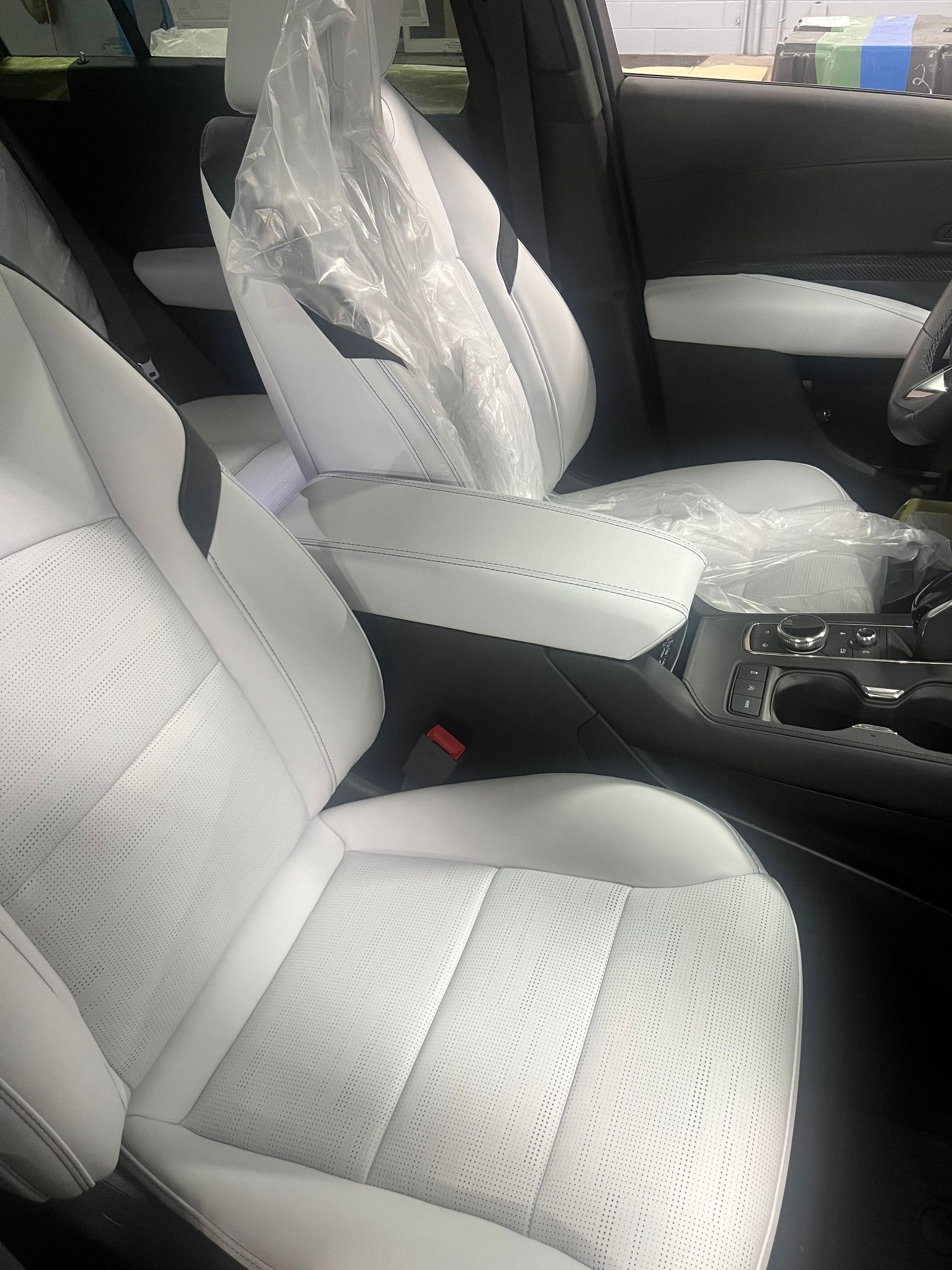 Car interior with white perforated leather seats and center console wrapped in protective plastic.