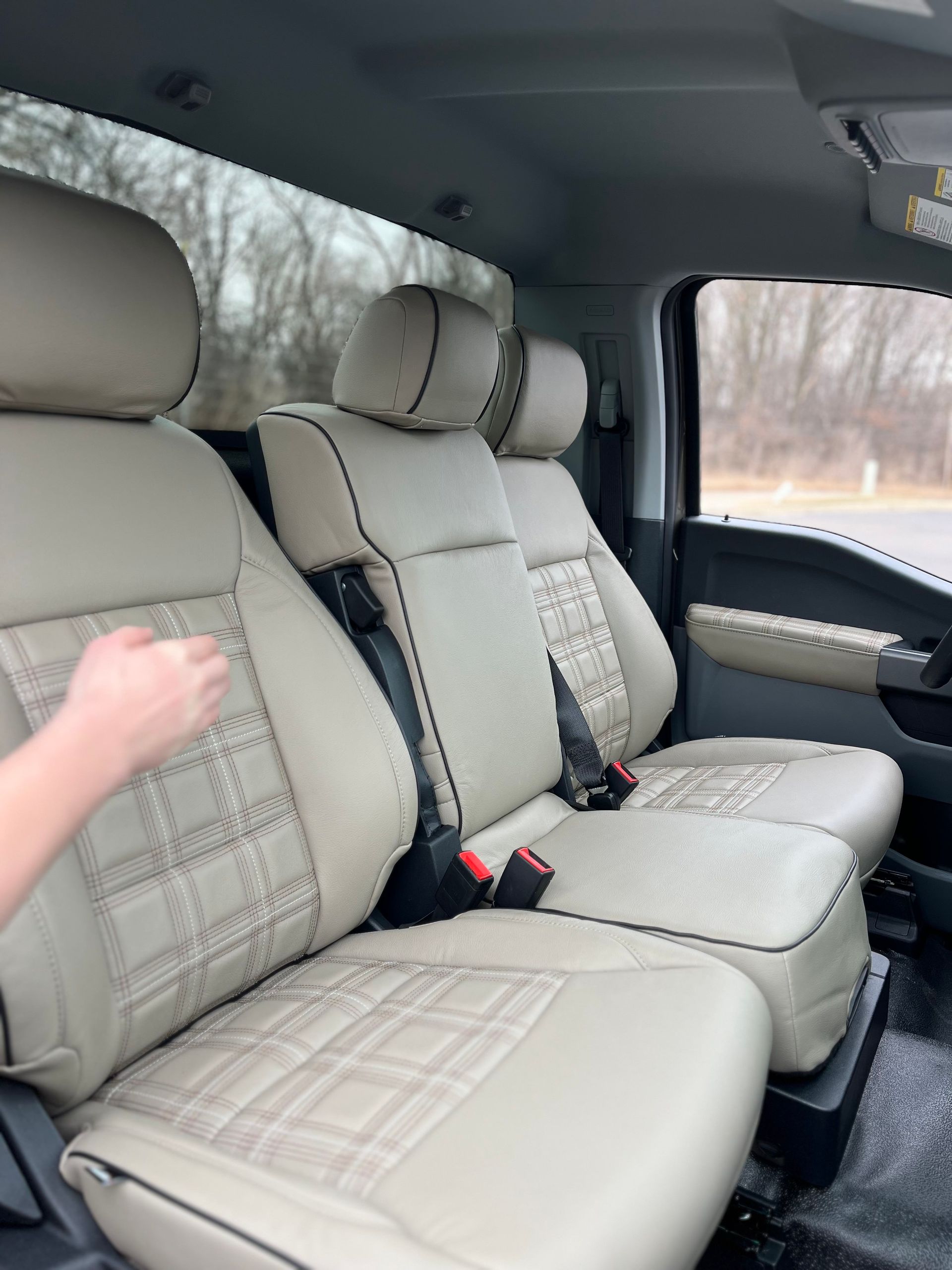 Beige leather car seats with headrests and a hand resting on the left seat in a vehicle interior