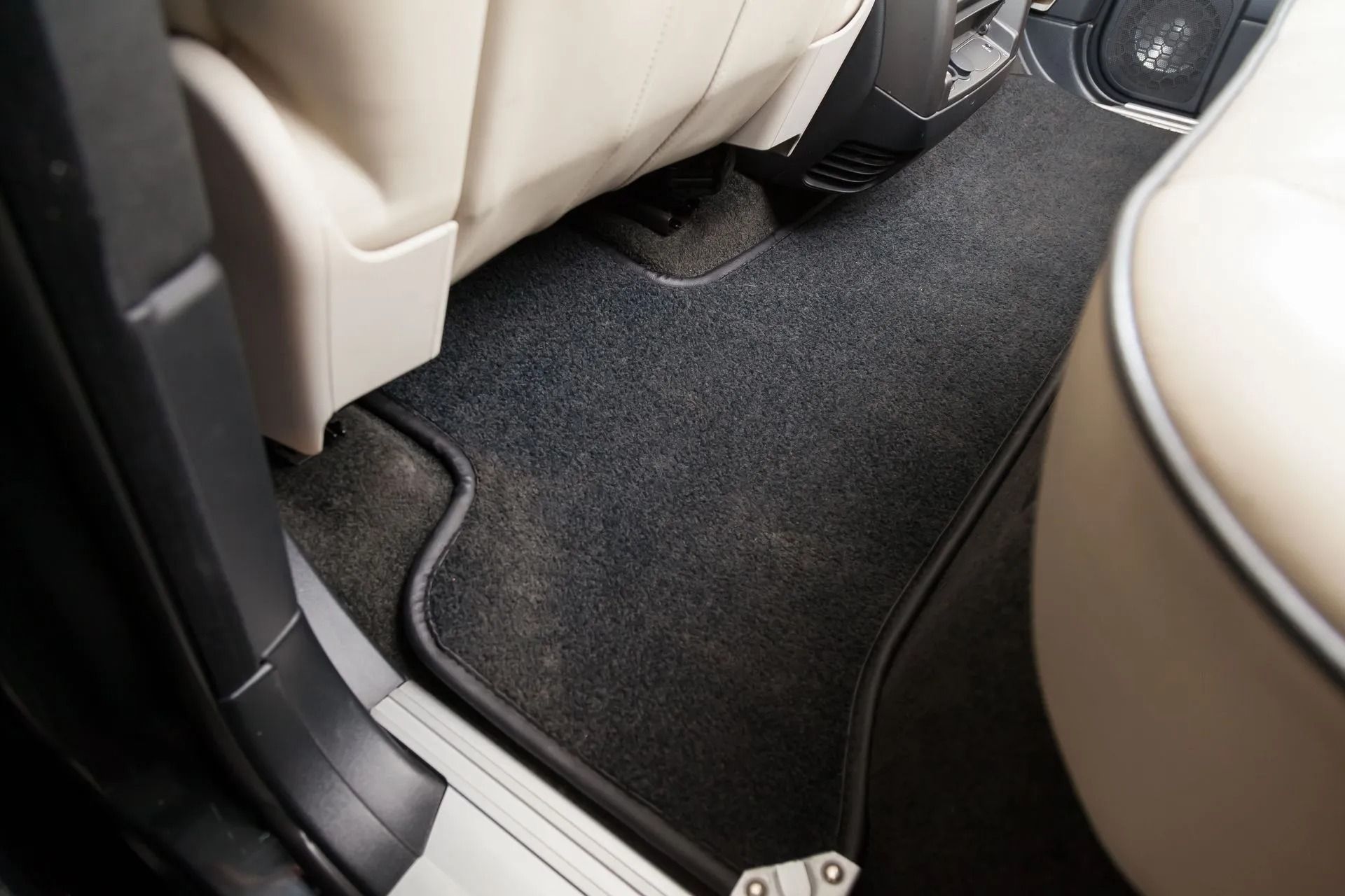 Car interior footwell with black carpet between beige seats and a door sill.