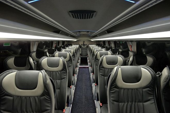 Empty bus interior with rows of gray seats and overhead lights in a modern coach