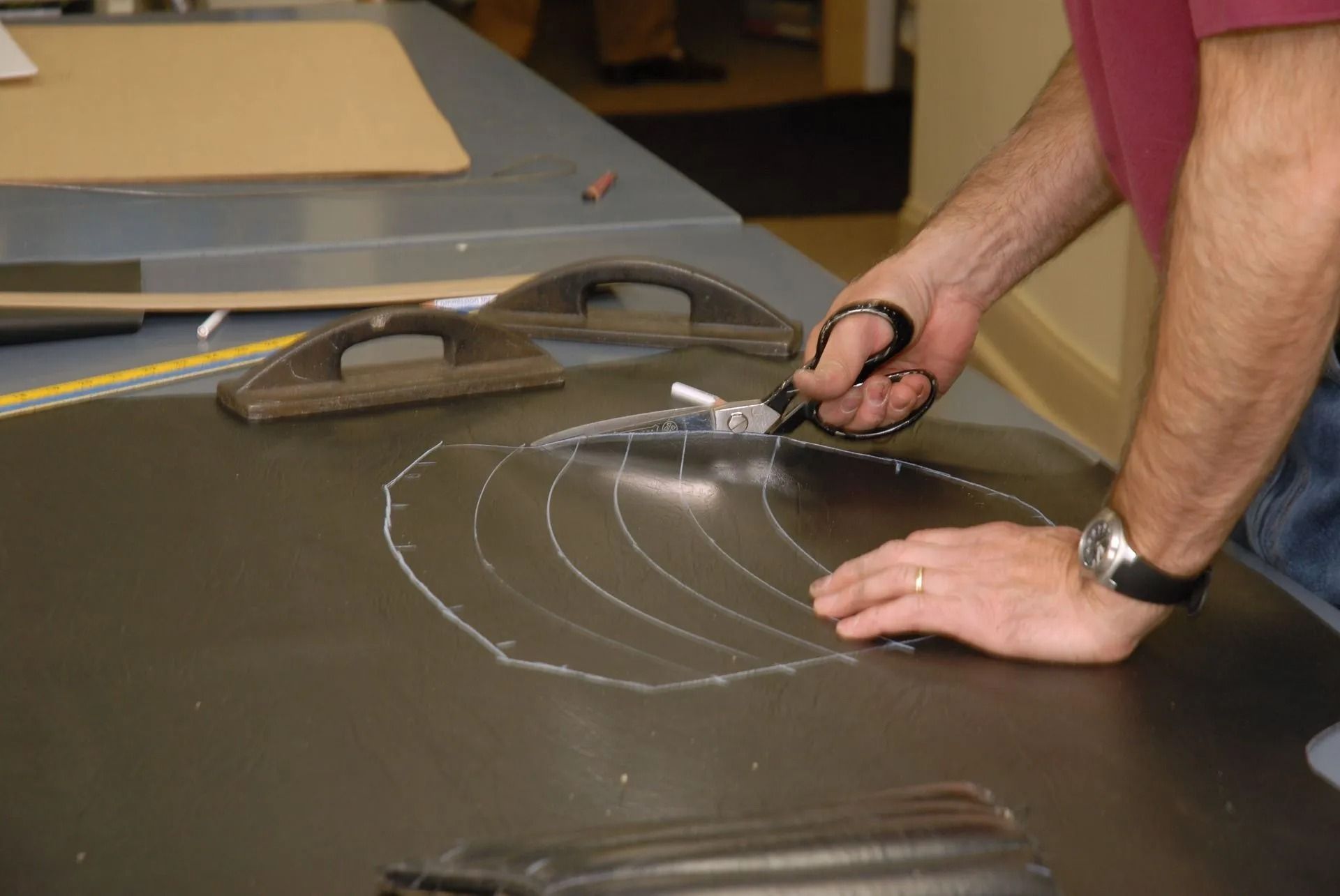 Person measuring a dark tabletop with a tape measure and chalk lines in a workshop