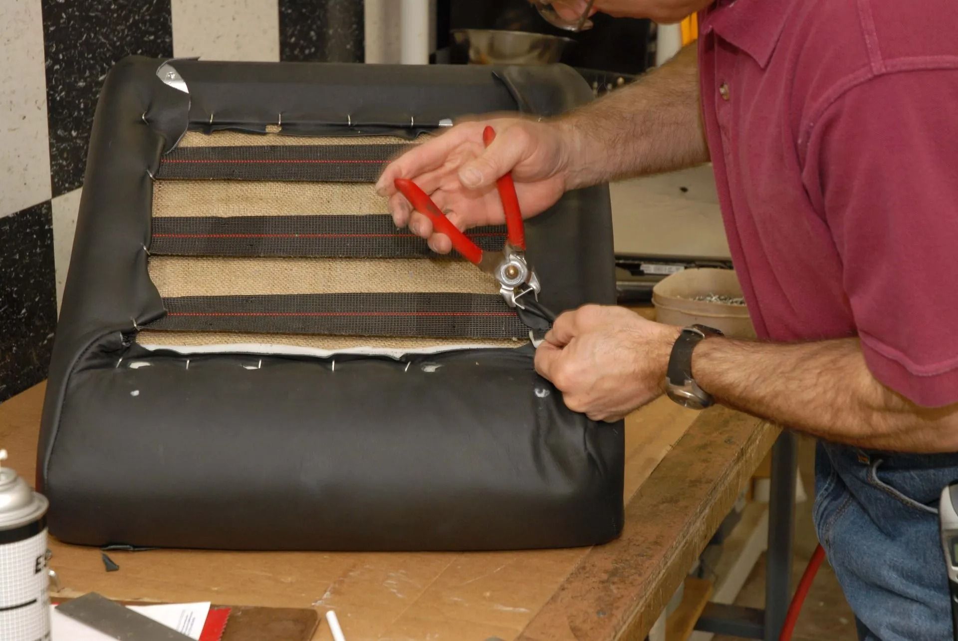 Person using pliers to repair a black leather chair cushion with exposed springs