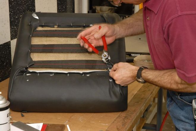 Person using pliers to repair a black leather chair cushion with exposed springs