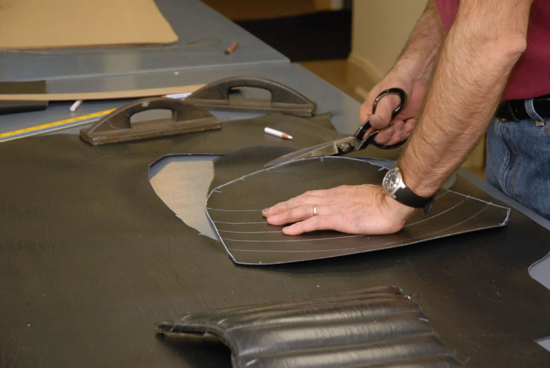 Person cutting black material with scissors on a worktable, with a leather car interior piece nearby