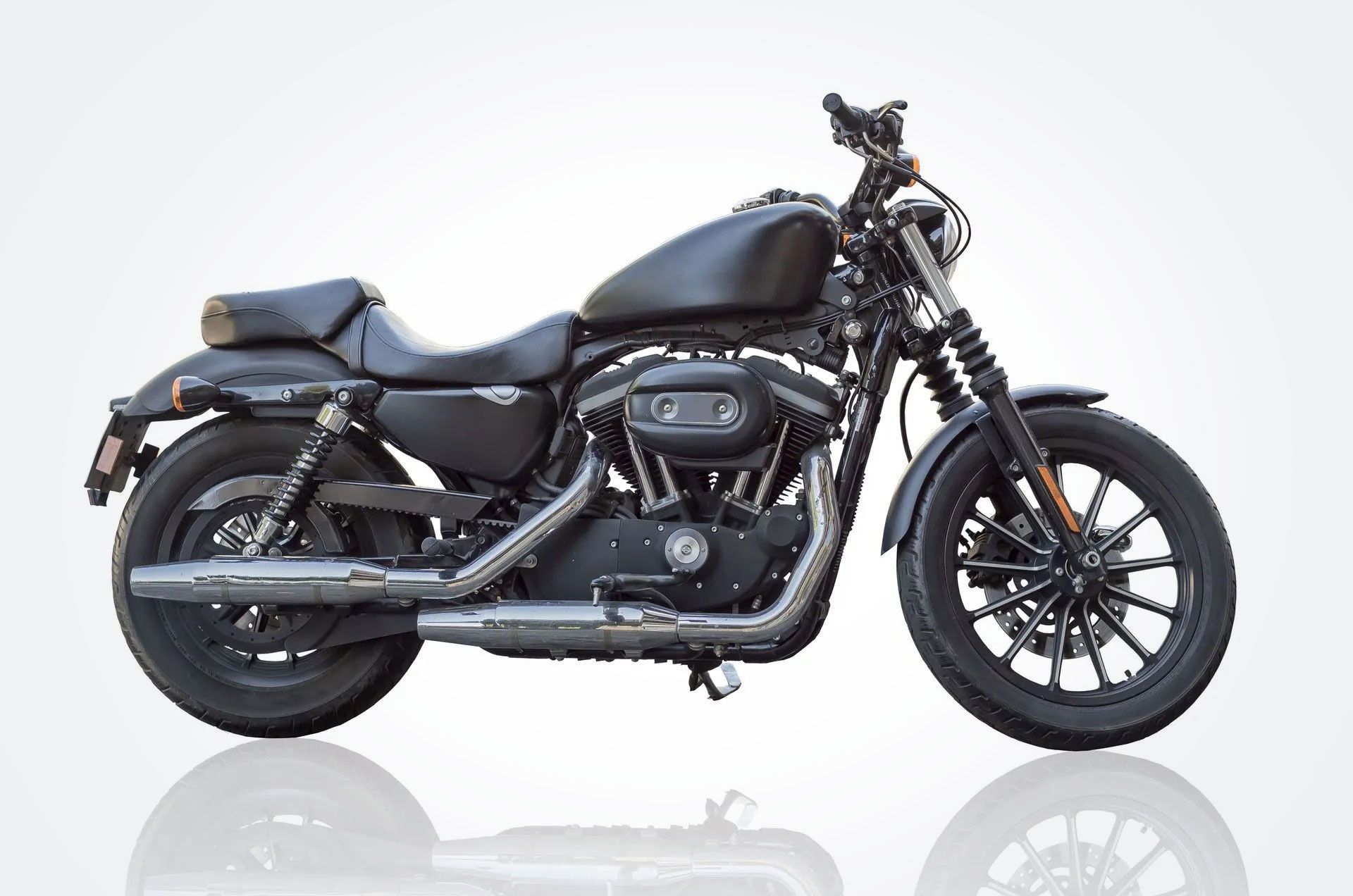 Black cruiser motorcycle on a white background, side view with chrome details and reflection