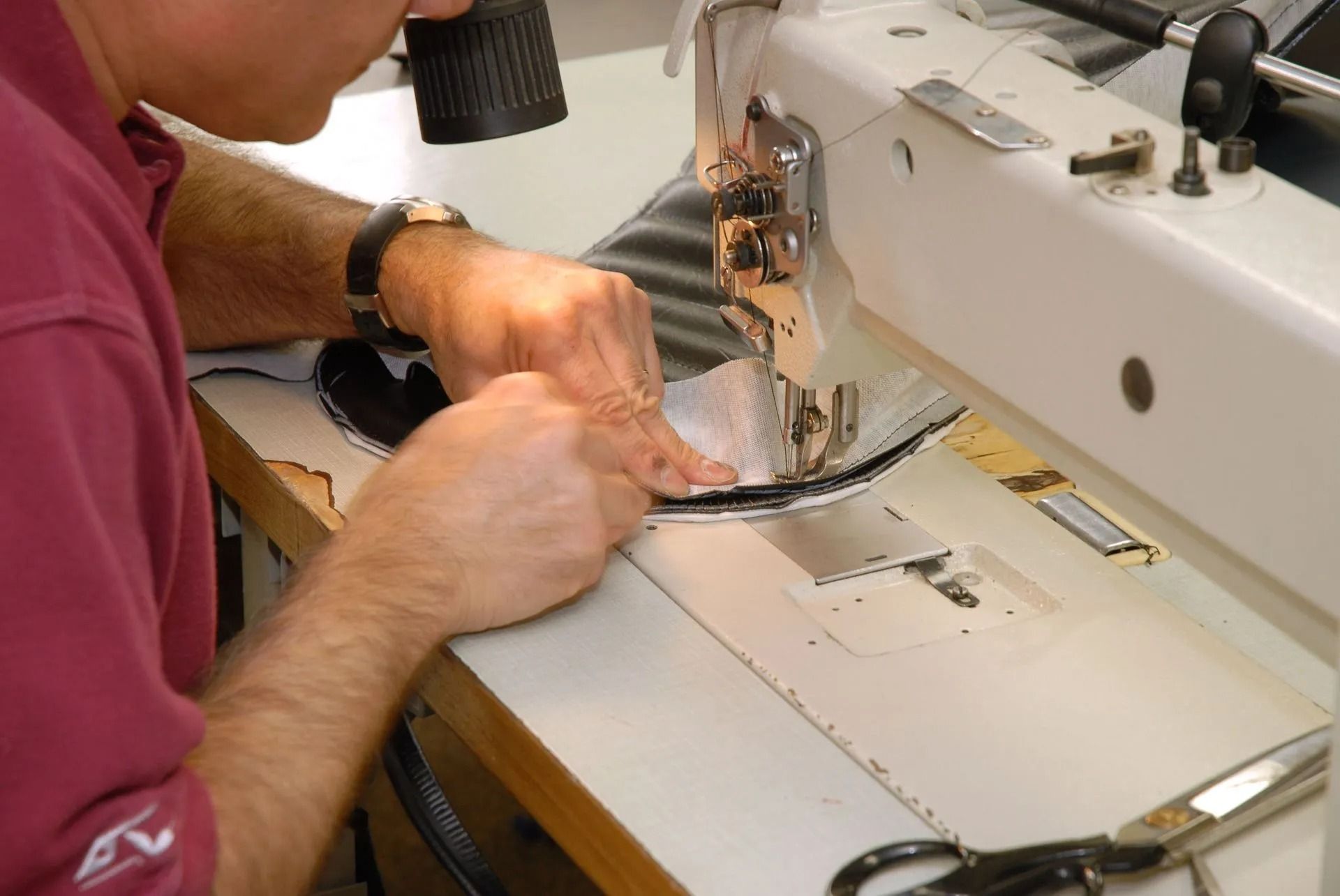 Person sewing fabric on a white sewing machine at a worktable.