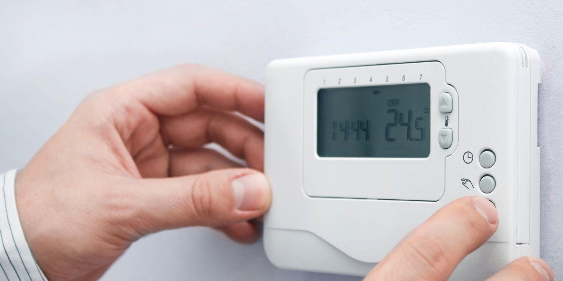 Person adjusting a white thermostat on a wall. The screen displays the time and temperature.