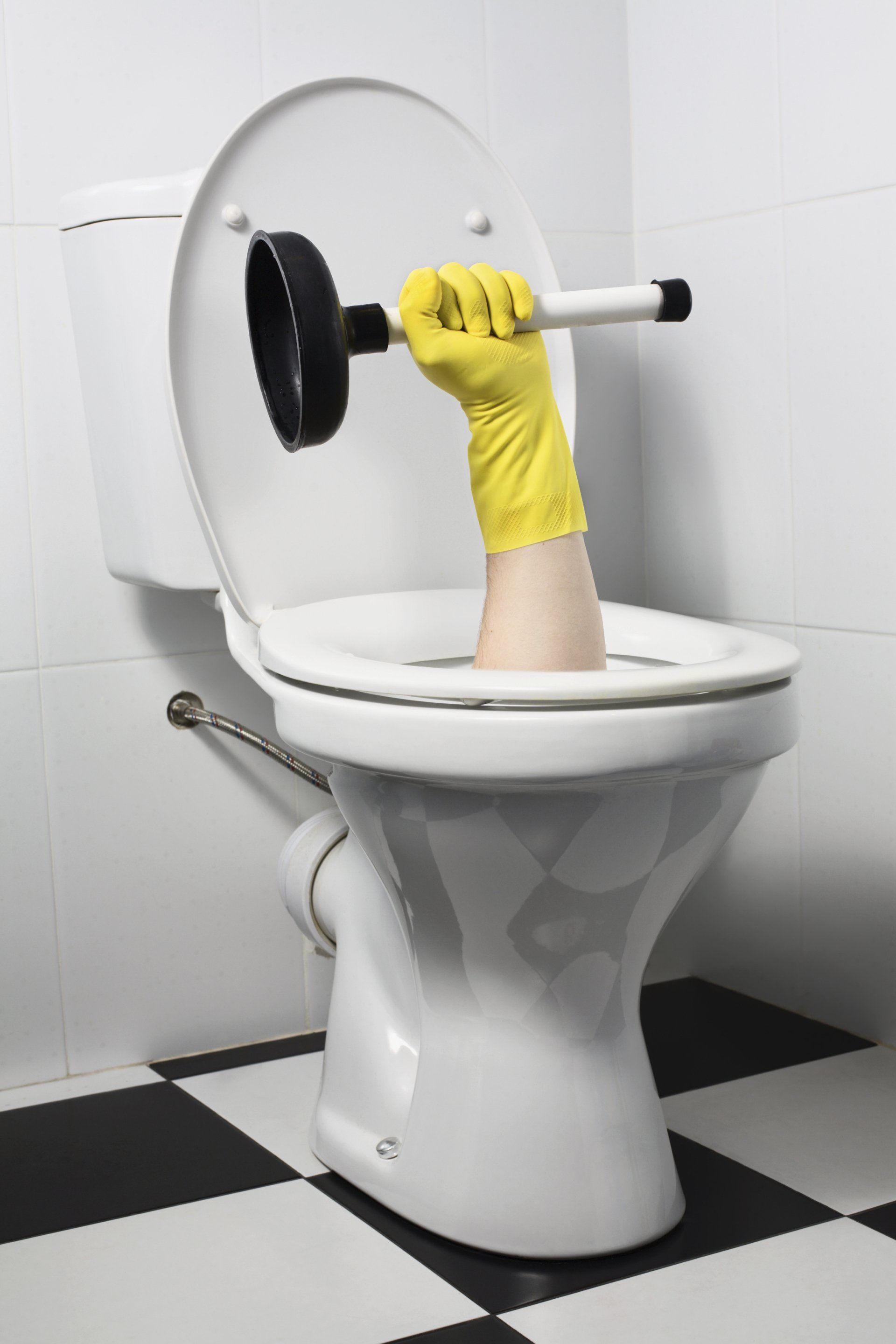 Hand in yellow glove plunges a toilet in a black and white tiled bathroom.