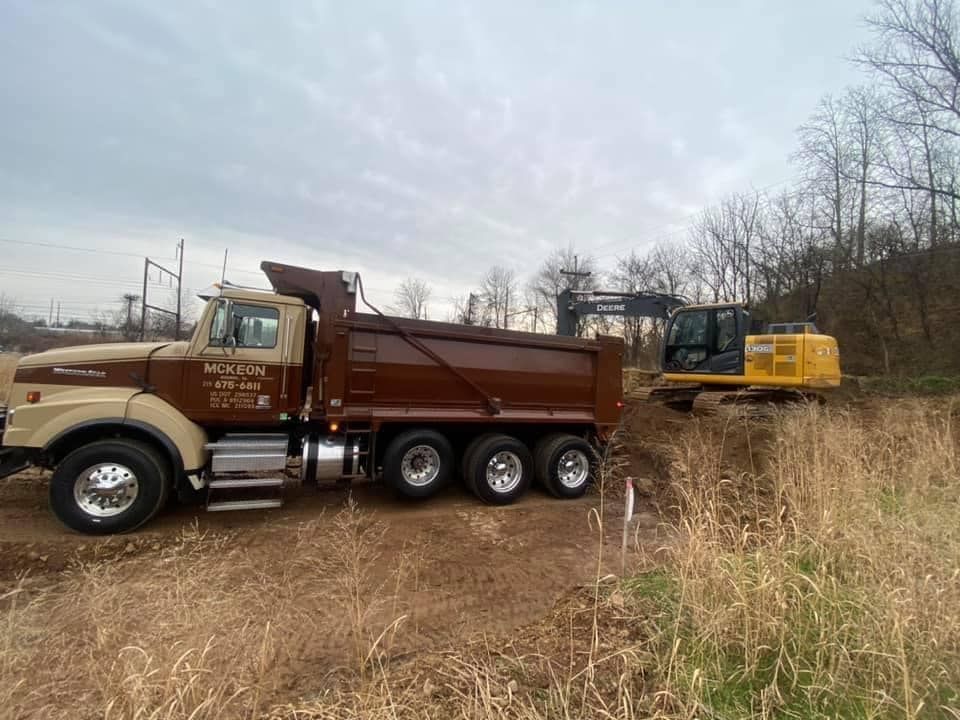 A dump truck is parked in a field next to a yellow excavator.