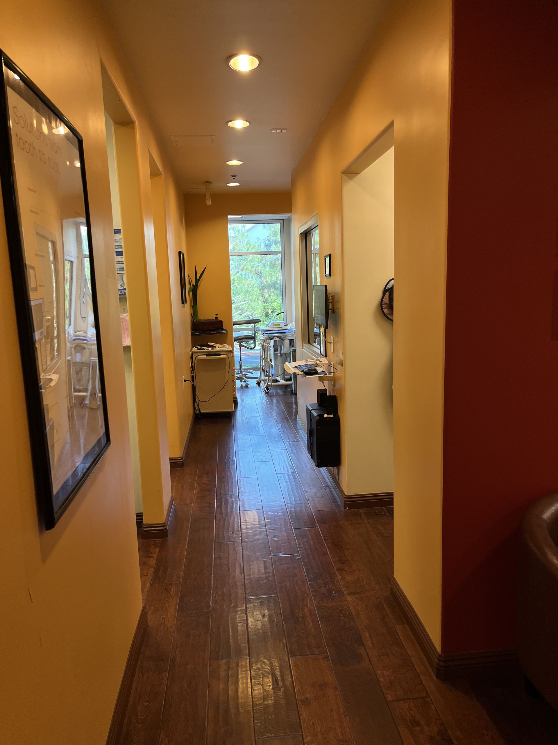 Narrow hallway with yellow walls, dark wood floor, and doorway to a bright room.