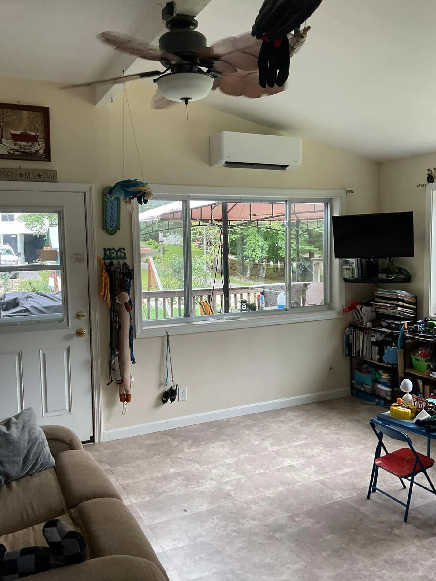 Tan living room with a beige sofa, window, TV, and a ceiling fan.