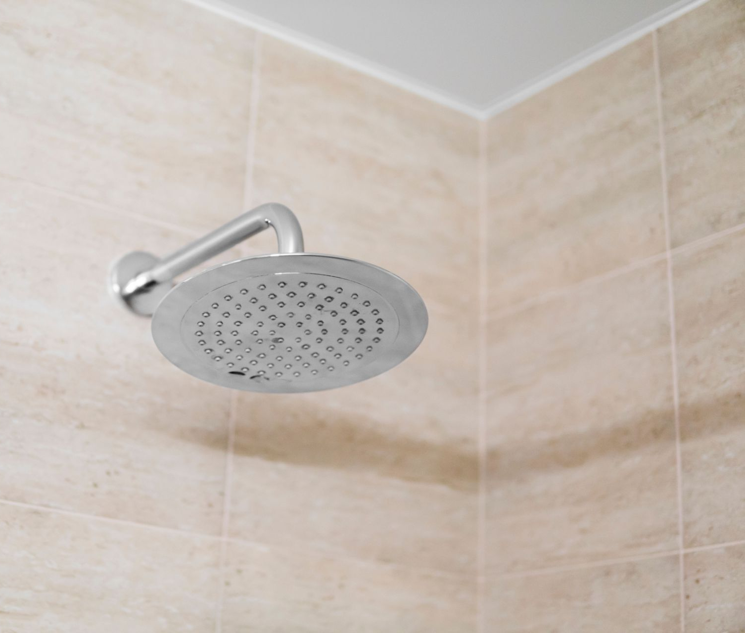Silver shower head mounted on a light-colored tiled wall.