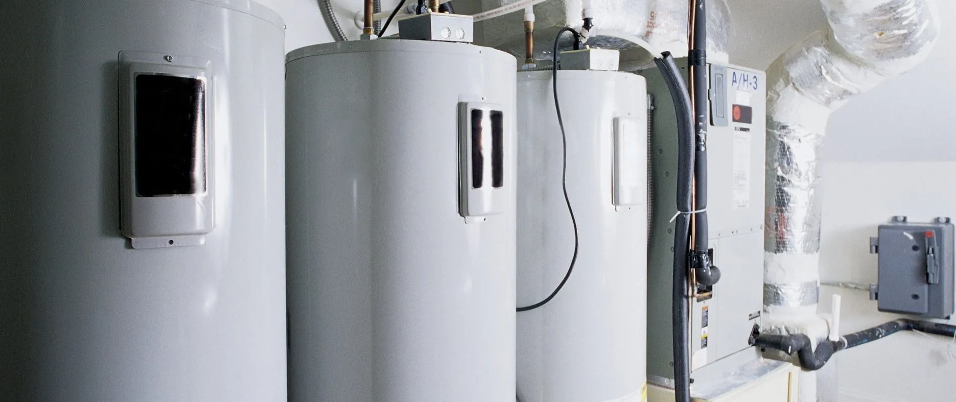 A row of white water heaters in a utility room.