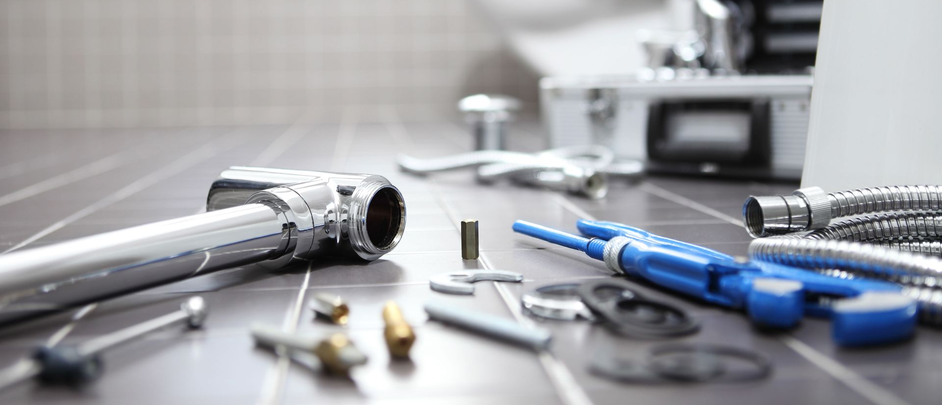 Close-up of plumbing tools on a tiled surface, including chrome pipes, wrenches, and blue tools.
