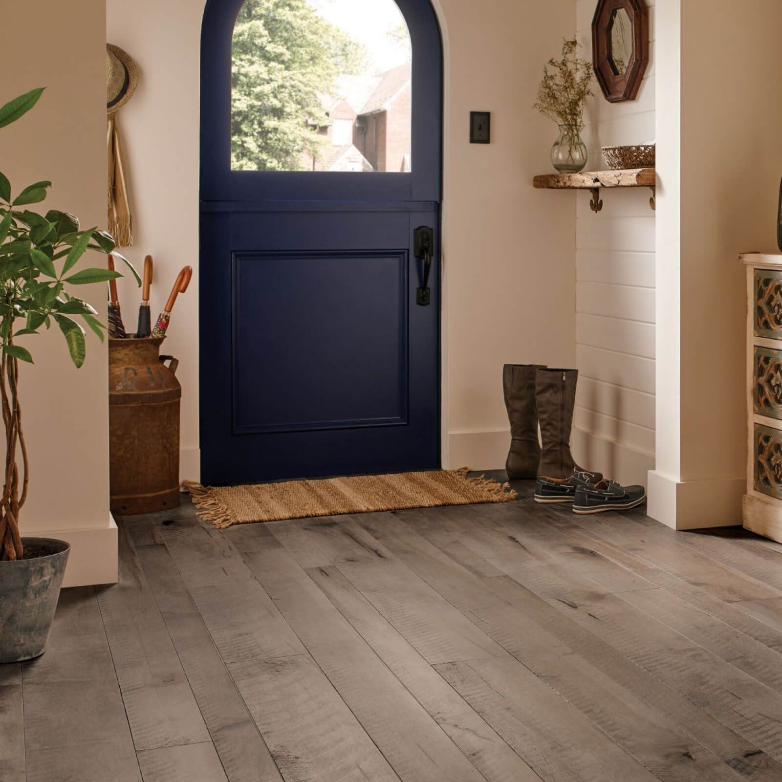 Entryway with blue door, gray wood floor, rug, boots, and plant.