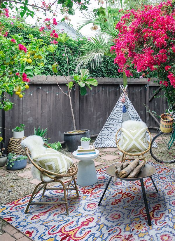 Cozy backyard scene with seating area, teepee, rug, flowers, and a bicycle.