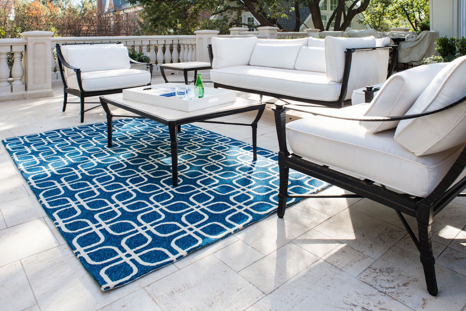 Outdoor patio furniture set on a blue patterned rug; white cushions, black frames.