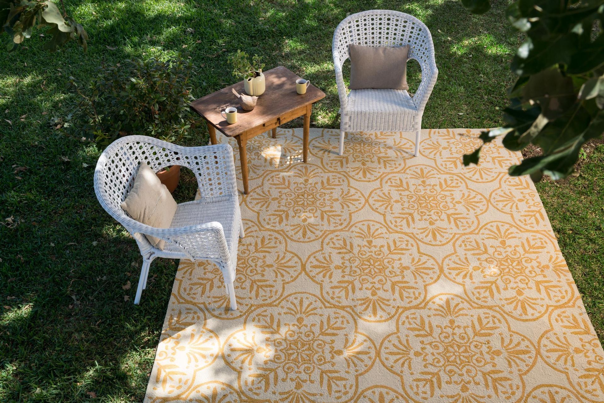White wicker chairs and small table on an outdoor rug, set on grass.
