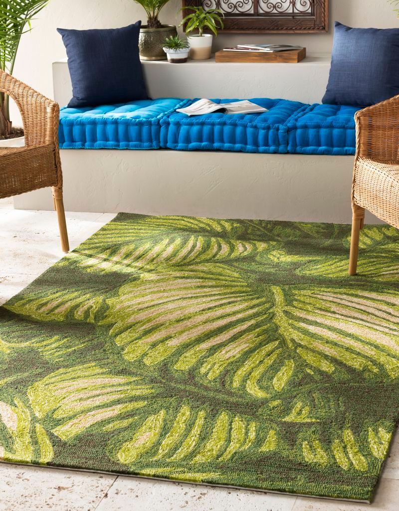 Green leaf-patterned outdoor rug with wicker chairs, blue cushions, and a built-in bench.