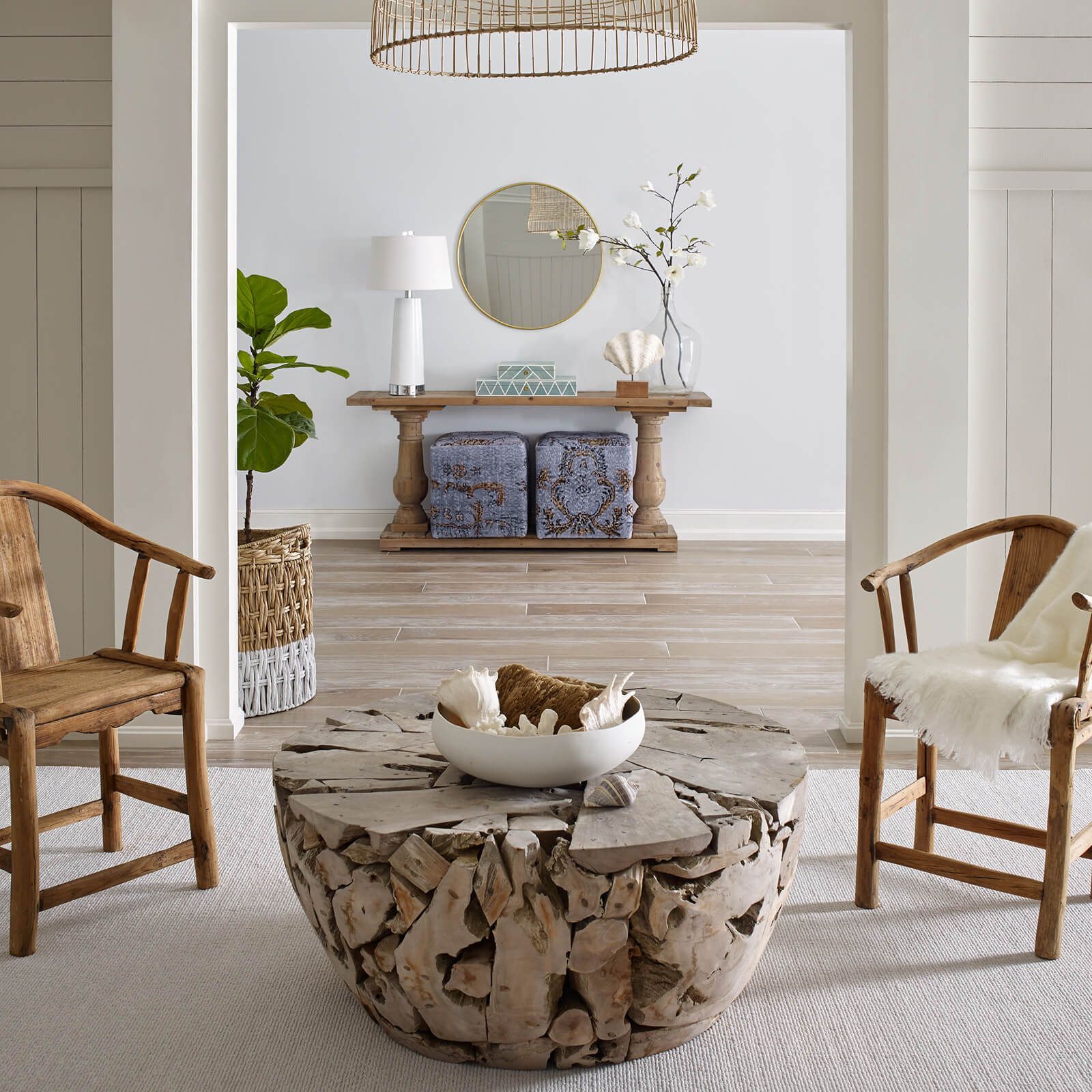 Coastal-style living room: wooden chairs, driftwood coffee table, console table with decor, and a white rug.
