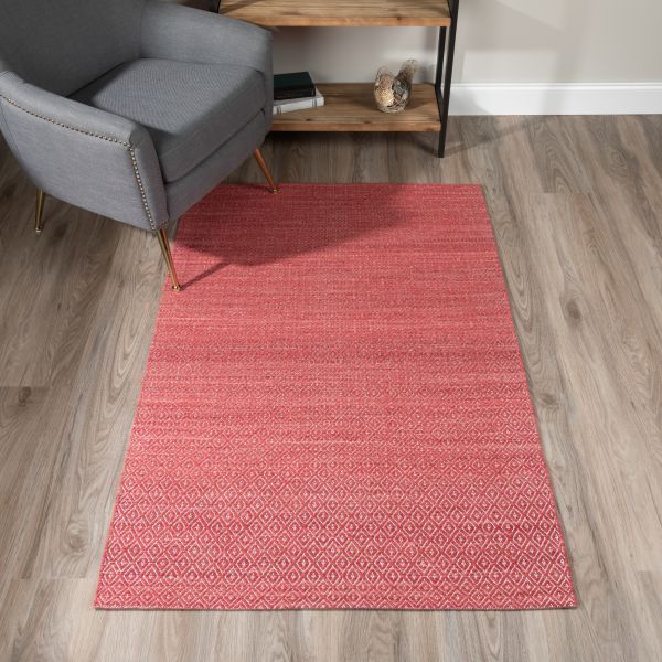 Red rectangular rug on light wood floor with a gray armchair and a wood shelf in the background.