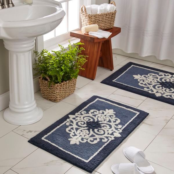 Two blue bath mats with white design in a bathroom with a sink and stool.