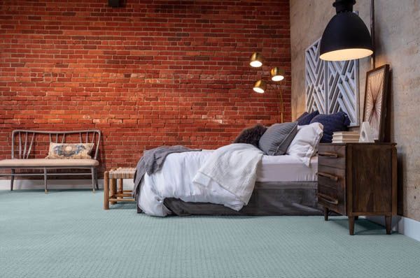 Bedroom with red brick wall, bed with white bedding, wooden furniture, and light blue carpet.