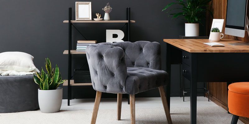 Grey upholstered chair in a home office with dark grey walls and a wooden desk.
