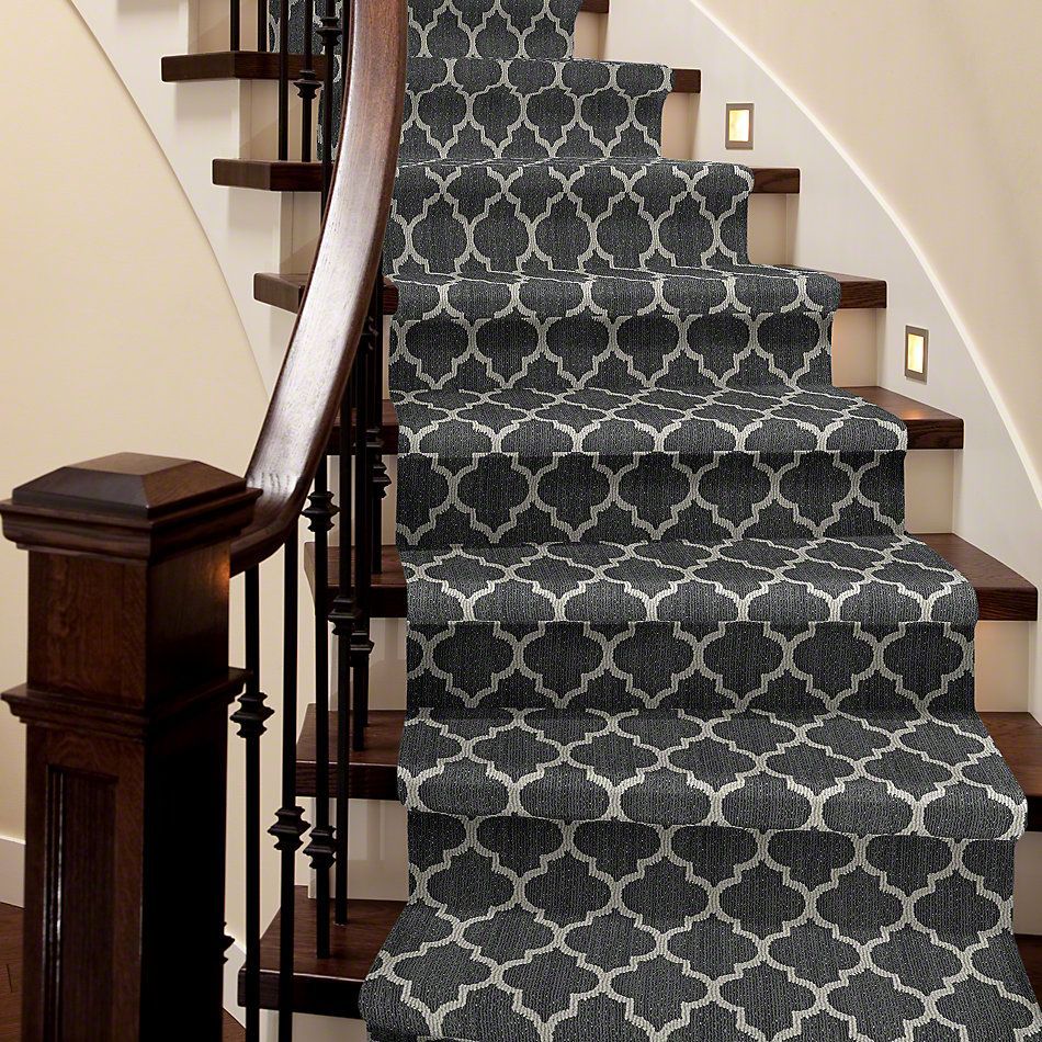 Staircase with dark wood banister and steps, covered with patterned charcoal and cream carpet.