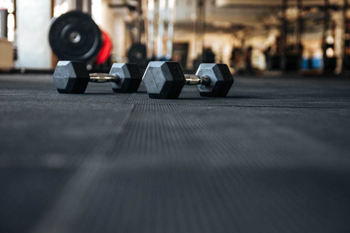 Two dumbbells on a black gym floor, blurred background of weights and equipment.