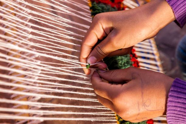 Hands weaving white thread into a loom, with colorful yarn visible.
