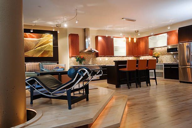 Modern kitchen and living space with dark wood cabinets, orange bar stools, and a chaise lounge.
