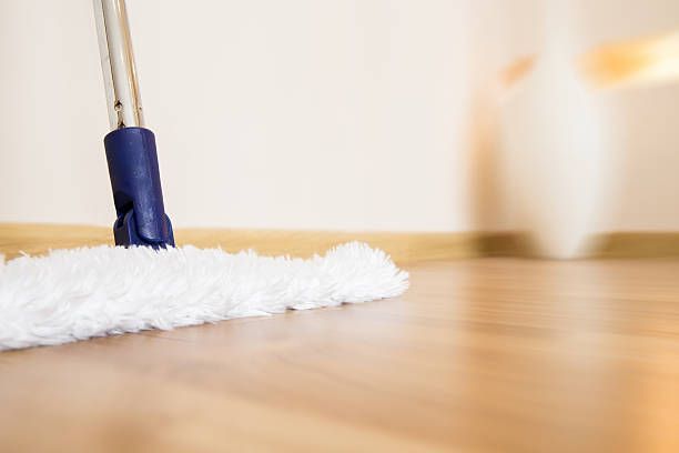 Mop cleaning a light-colored wooden floor near a beige wall.