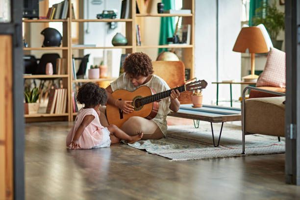 Person playing acoustic guitar for child indoors.