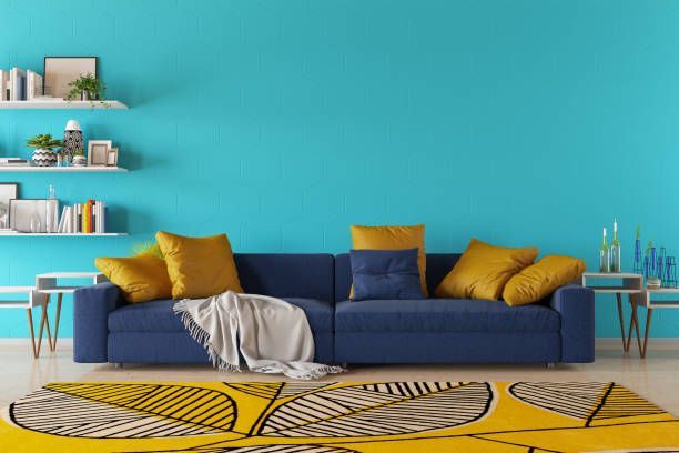 Blue couch with yellow pillows, a beige blanket, and a yellow rug against a turquoise wall.
