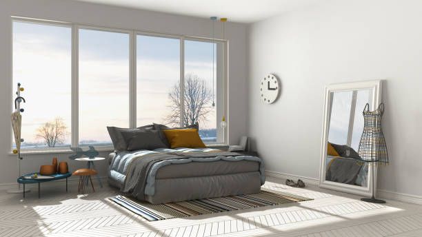 Bright bedroom with bed, large window overlooking winter landscape, full-length mirror, clock, and rug.