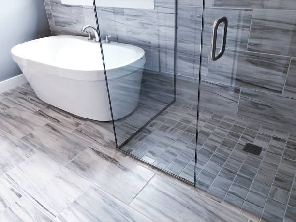 Modern bathroom with gray and white marbled tile, glass shower, and white soaking tub.