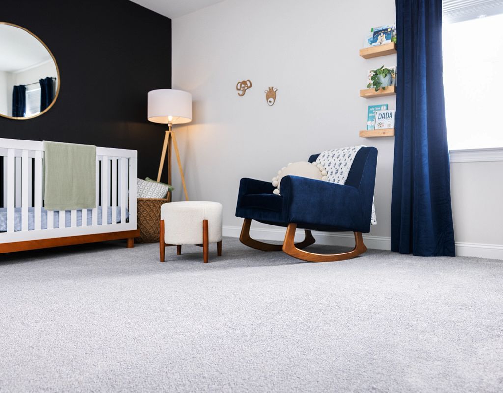 Nursery with crib, rocking chair, and shelves, in a room with a black accent wall and light-colored carpet.