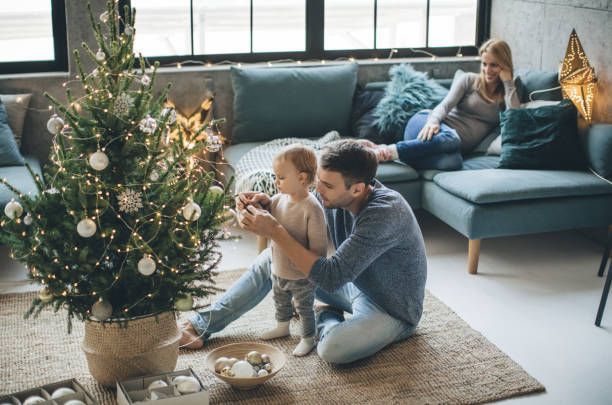 Father and child decorating Christmas tree; mother relaxes on couch.