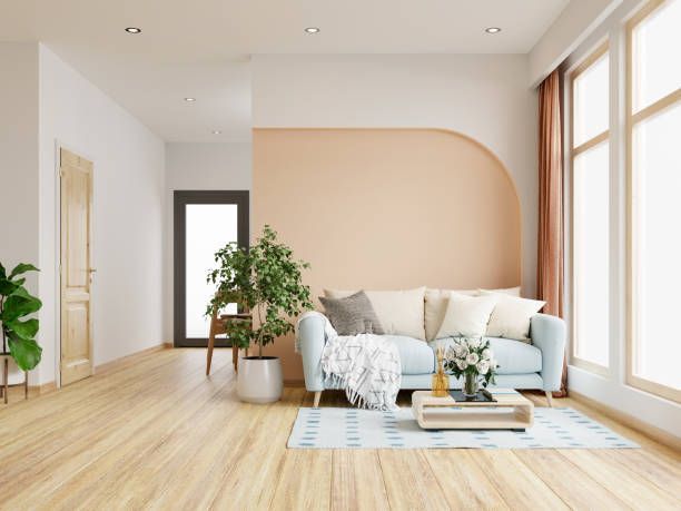 Light-filled living room with light blue sofa, peach accent wall, large windows, wood flooring, and indoor plants.
