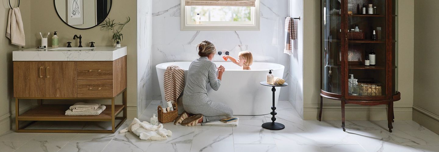 Woman and child in a modern bathroom, woman kneels near a bathtub playing with a child.